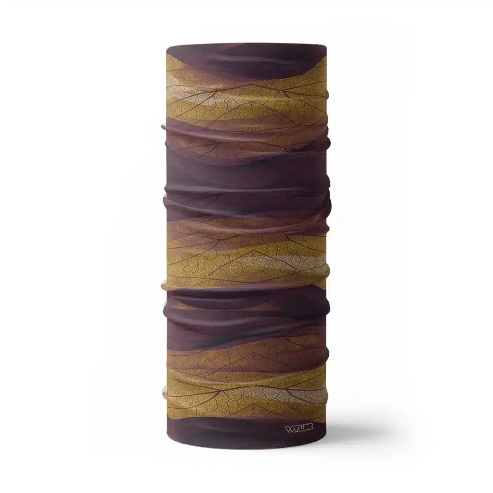 an image of a full neck gaiter. The design features lines and breaks to recreate the look of a leaf print. The colors behind the print mimic waves. This image showcases colors in warm purples, yellows and oranges.