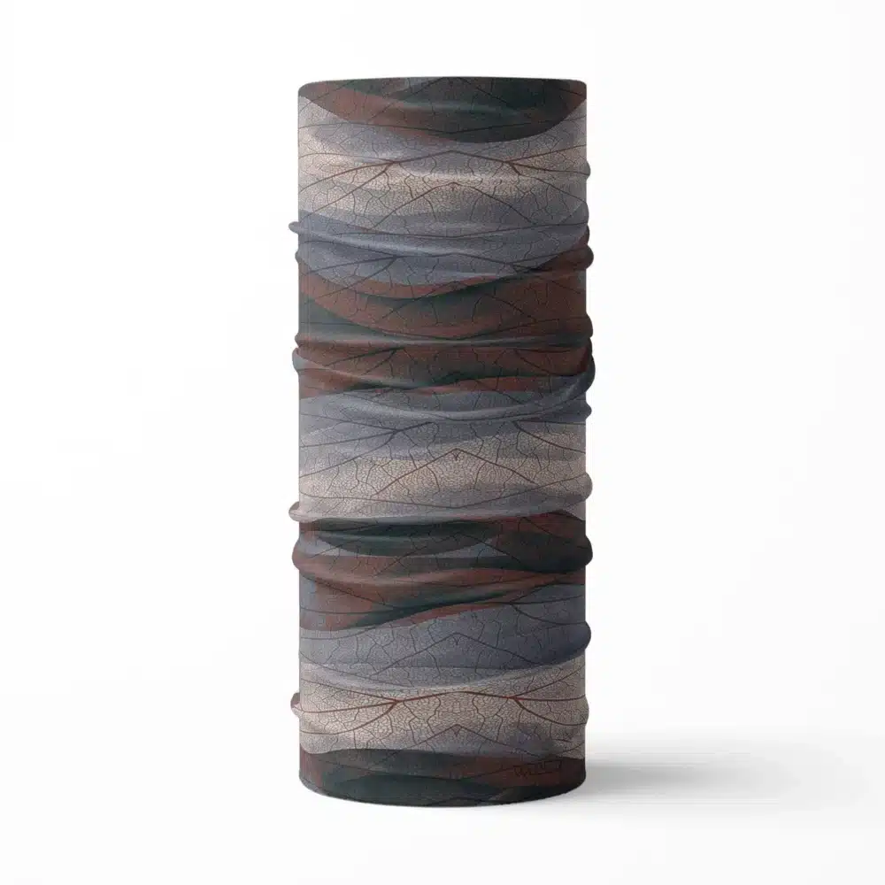an image of a full neck gaiter. The design features lines and breaks to recreate the look of a leaf print. The colors behind the print mimic waves. This image showcases colors in cool reds, grays and blues.