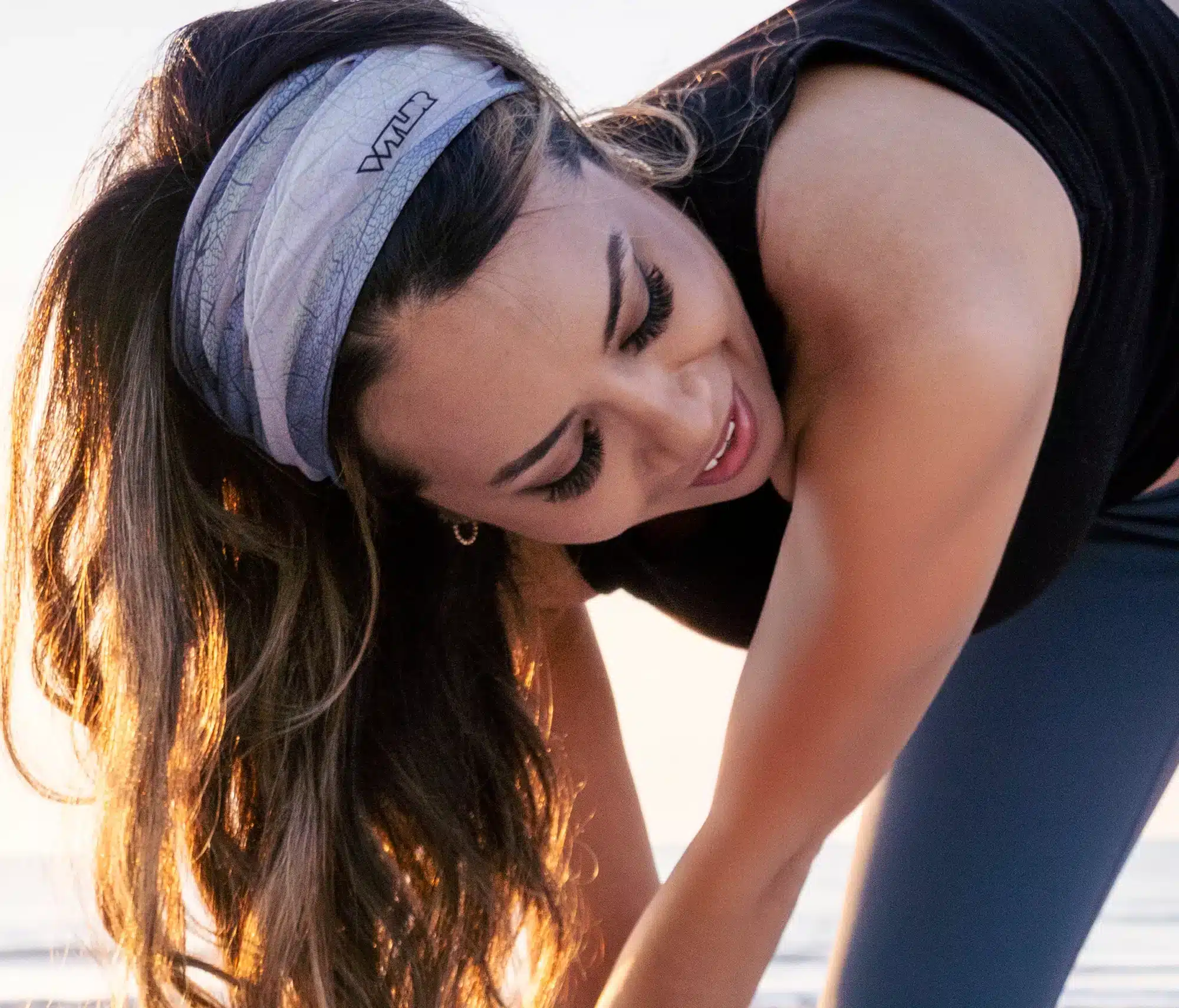 An image of a person wearing a wide sports headband while doing a yoga pose. The headband is of a fractured leaf print in several shades of blues and purples.