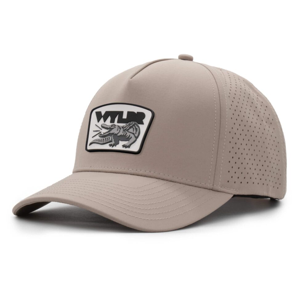 three-quarter view of a 5 panel, water resistant, floatable hat with a PVC patch. the patch is a gator catching a golf ball in its mouth and features the brand name, Wyldr. the hat is a warm tan color