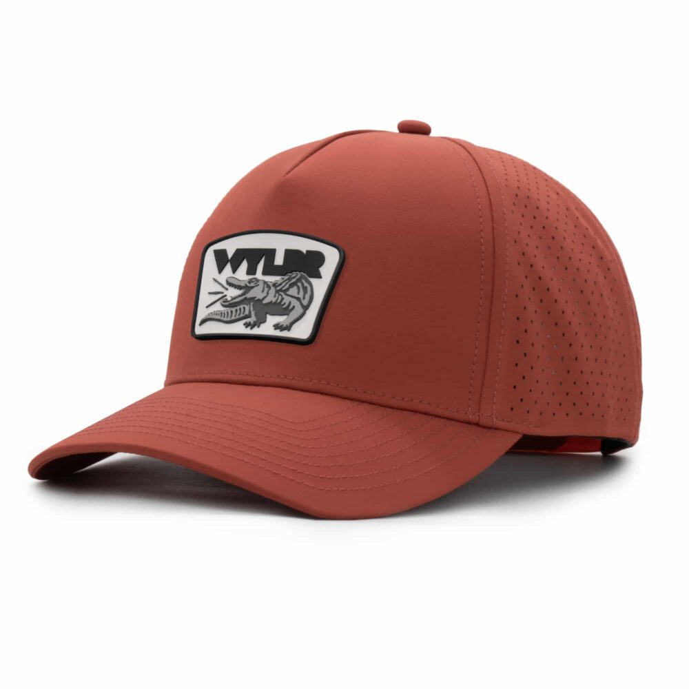 three-quarter view of a 5 panel, water resistant, floatable hat with a PVC patch. the patch is a gator catching a golf ball in its mouth and features the brand name, Wyldr. the hat is a rusty-orange color