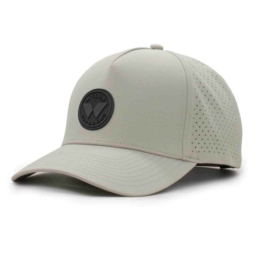 three-quarter view of a 5 panel, water resistant, floatable hat with a PVC patch. the patch is a round medallion featuring the letter W and the text Wyldr Outdoors. the hat is light tan
