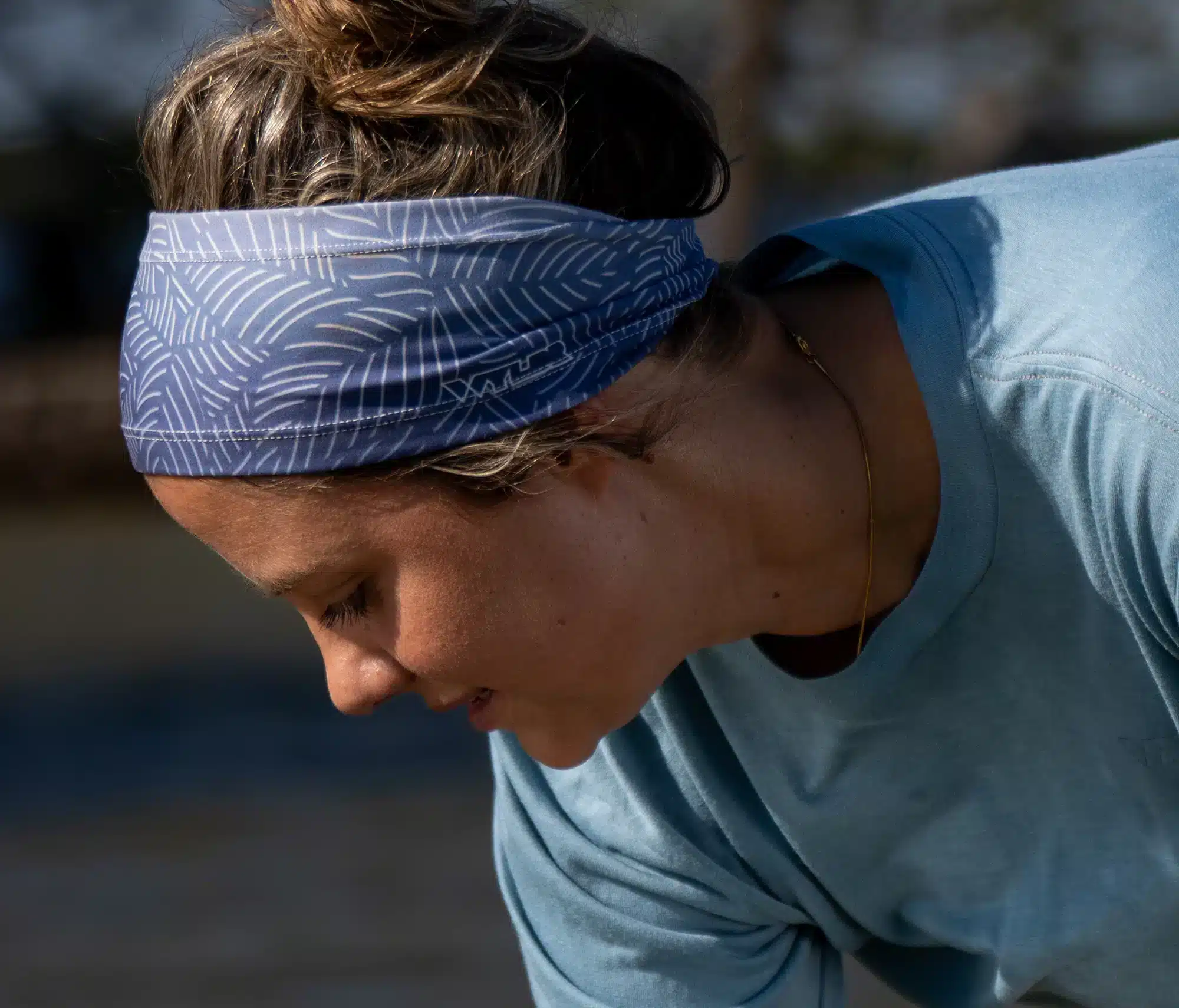 An image of a person wearing a tapered sports headband. It's a gradient blue with a white leaf print.